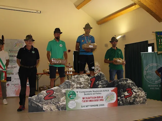 Siegerehrung einer Kategorie bei der 9. Nationalen ANA-Mountainbike-Meisterschaft in Cesiomaggiore, mit den Athleten auf dem Podest und den Alpini-Wimpeln im Hintergrund