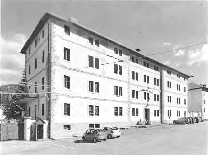 Palazzina di quattro piani della caserma Calbo a Santo Stefano di Cadore, con auto parcheggiate davanti, in bianco e nero