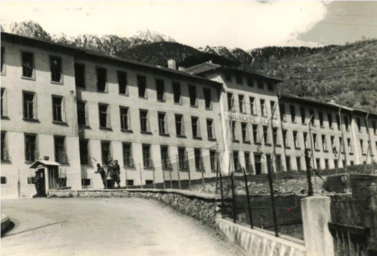 Il grande edificio a quattro piani della caserma De Gol visto dalla strada provinciale, con le montagne sullo sfondo