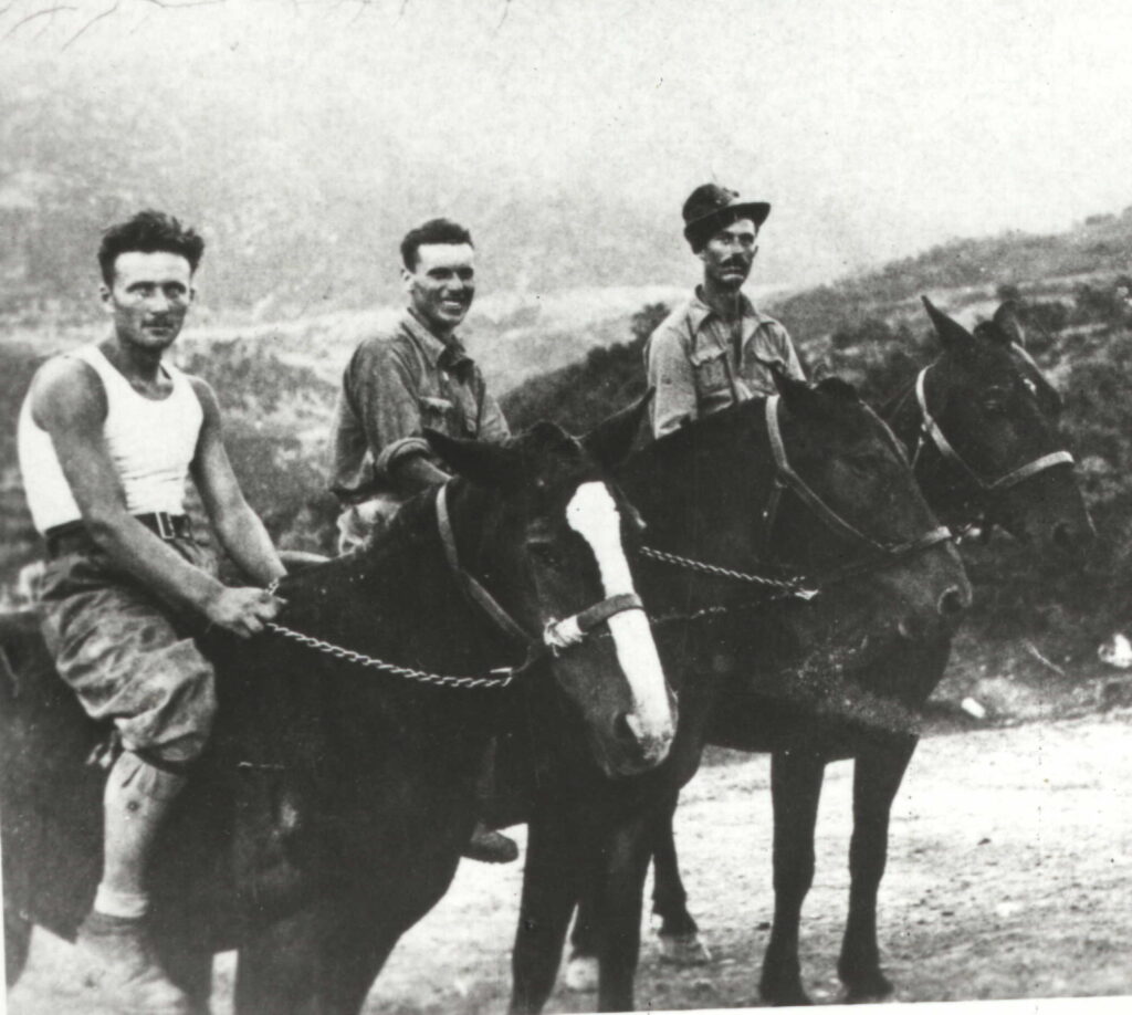 Tre militari a cavallo su un sentiero di montagna: a sinistra un uomo in canottiera