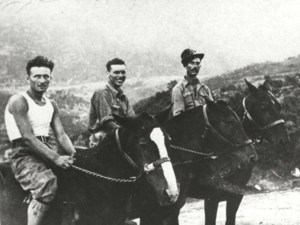 Tre militari a cavallo su un sentiero di montagna: a sinistra un uomo in canottiera