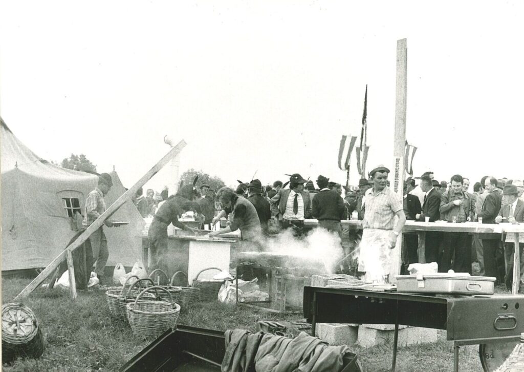 Alpini al lavoro alle cucine da campo durante la festa sul Col Maòr, con la folla sullo sfondo