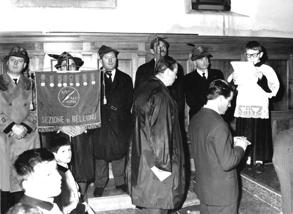 Alpini e sacerdote davanti al vessillo della Sezione ANA di Belluno durante la cerimonia di inaugurazione del Gruppo di Salce, 1964