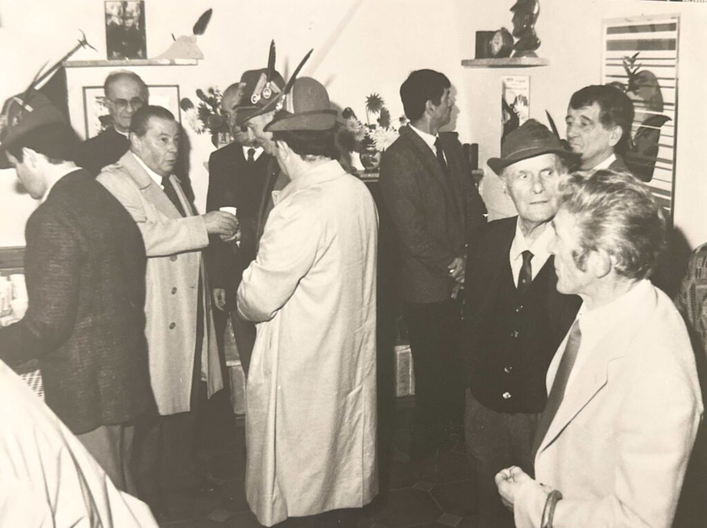 Alpini con il cappello e ospiti brindano in una stanza affollata durante l’inaugurazione della prima sede del Gruppo