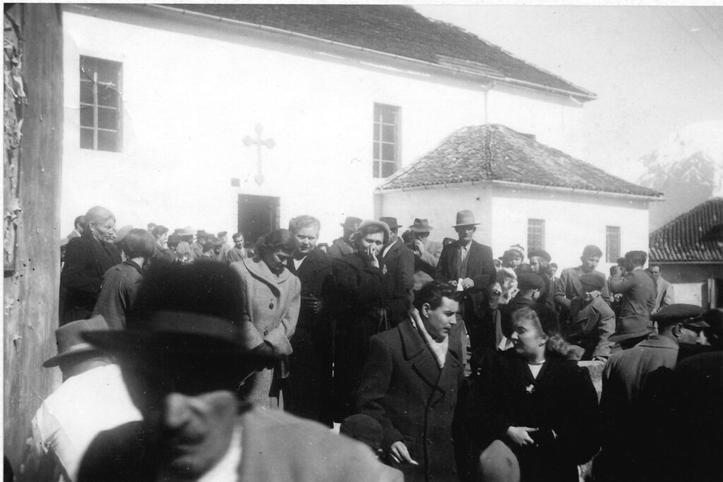 Folla di uomini e donne con cappotti e cappelli davanti alla facciata bianca della chiesa