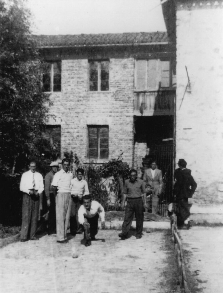 Uomini che giocano a bocce davanti a una casa in pietra a tre piani, nel 1941