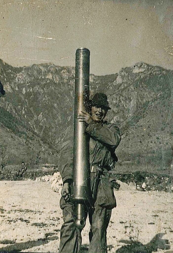 Toni Tamburlin, giovane artigliere da montagna, tiene in piedi la bocca da fuoco di un mortaio su un piazzale di montagna, 1964