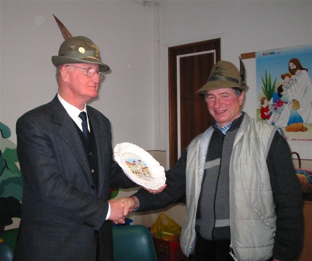 Il presidente sezionale Arrigo Cadore consegna un piatto in ceramica a Toni Tamburlin, con il cappello alpino e un gilet chiaro, all’assemblea del 2003