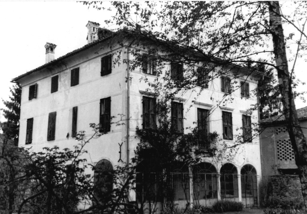 Grande villa a tre piani con porticato ad archi al piano terra, parzialmente coperta da alberi