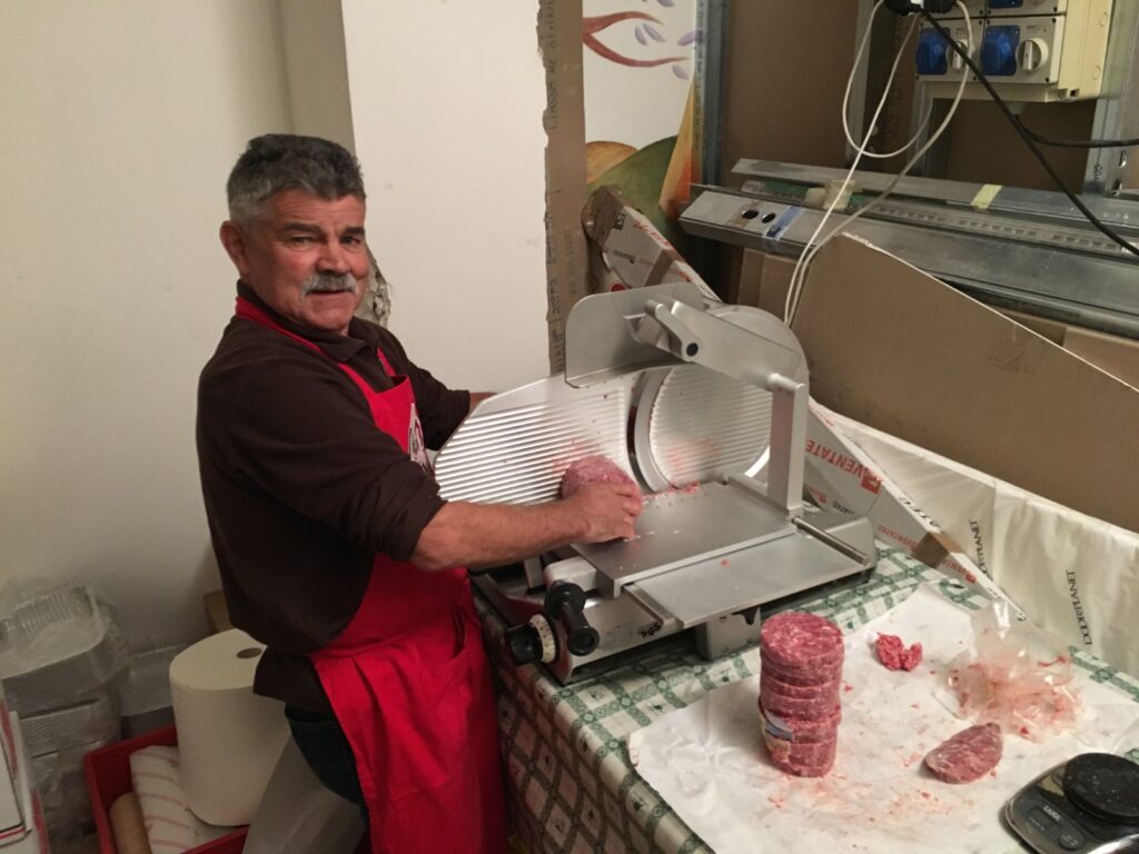 Our dear friend Rasa (who has since passed away), in a red apron, shaping pastìn patties with the press inside the stand.