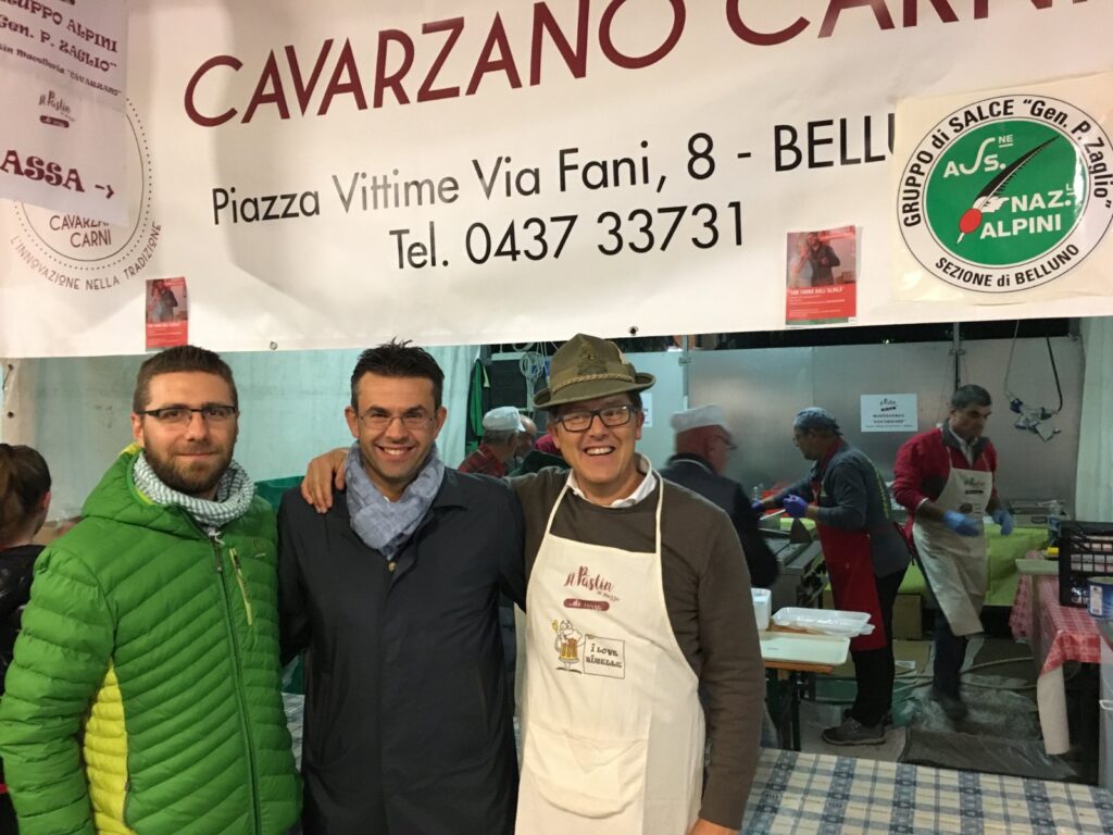 From left: Marco Bogo (Belluno city councillor for sport and leisure), Roberto Padrin (President of the Province) and Michele Sacchet (in charge of the bar with the volunteers), in front of the Cavarzano Carni stand with the banner of the Salce Alpini Group.