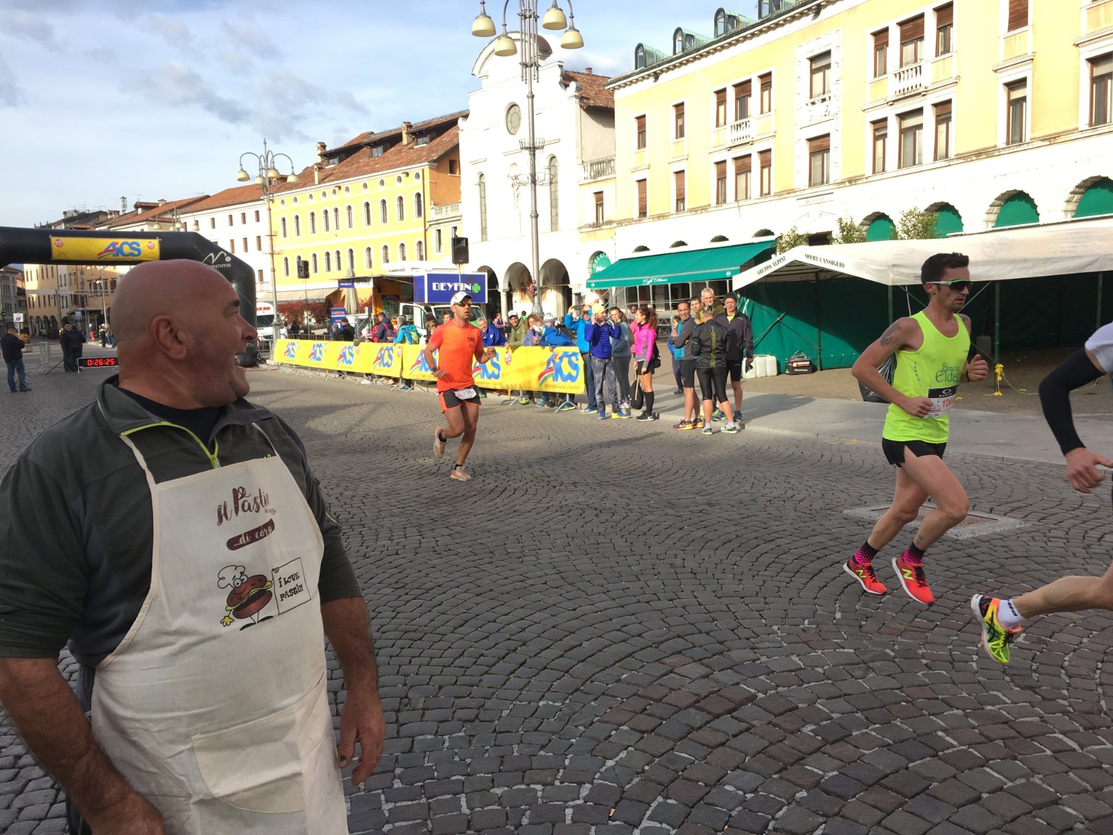 Corridori passano in Piazza dei Martiri davanti a un volontario in grembiule